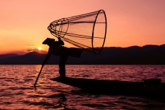 Silhouette of a traditional Burmese fisherman on Inle Lake at sunset in Myanmar.