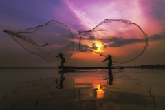 Silhouette of asia traditional fisherman in action when fishing at sunrise